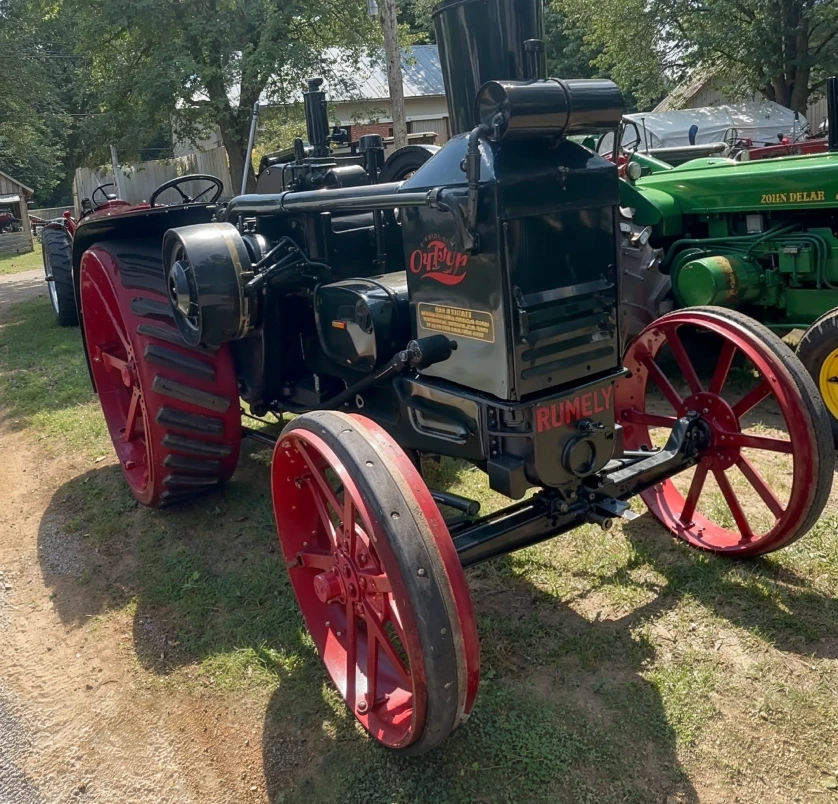 Vintage Rumely oil-pull tractor with red metal wheels and black body parked on grass.