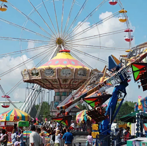 People enjoying rides at a carnival featuring a colorful swing carousel and a large Ferris wheel against a blue sky with clouds.