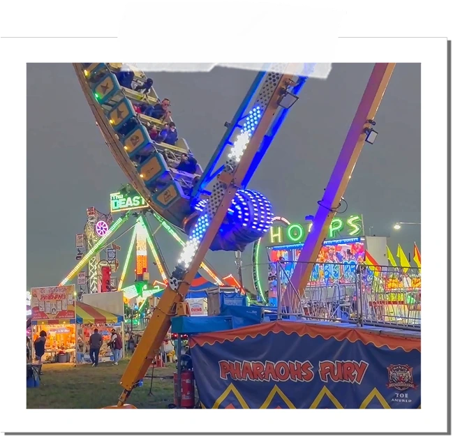 A carnival ride named Pharaoh's Fury swinging with riders on board at an outdoor fair during evening, colorful lights and other rides visible in the background.