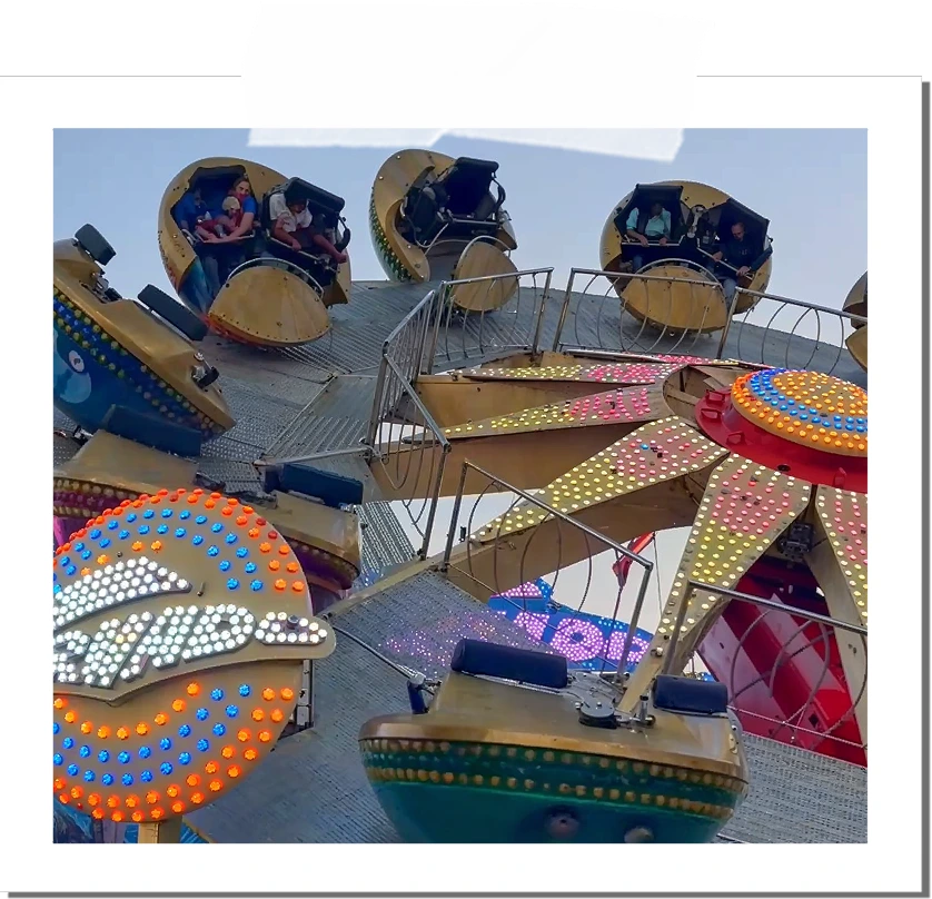 People seated in individual circular cars on a spinning amusement park ride with colorful lights against a clear sky.