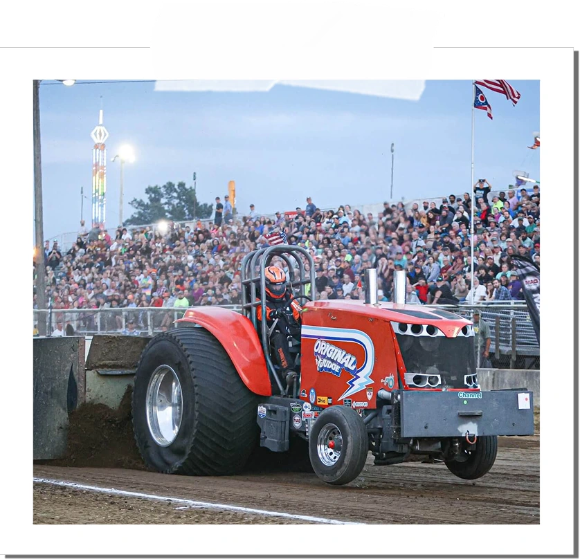 Orange pull tractor labeled Original Fudge with a driver wearing an orange and black helmet at a tractor pull event in front of a packed crowd.