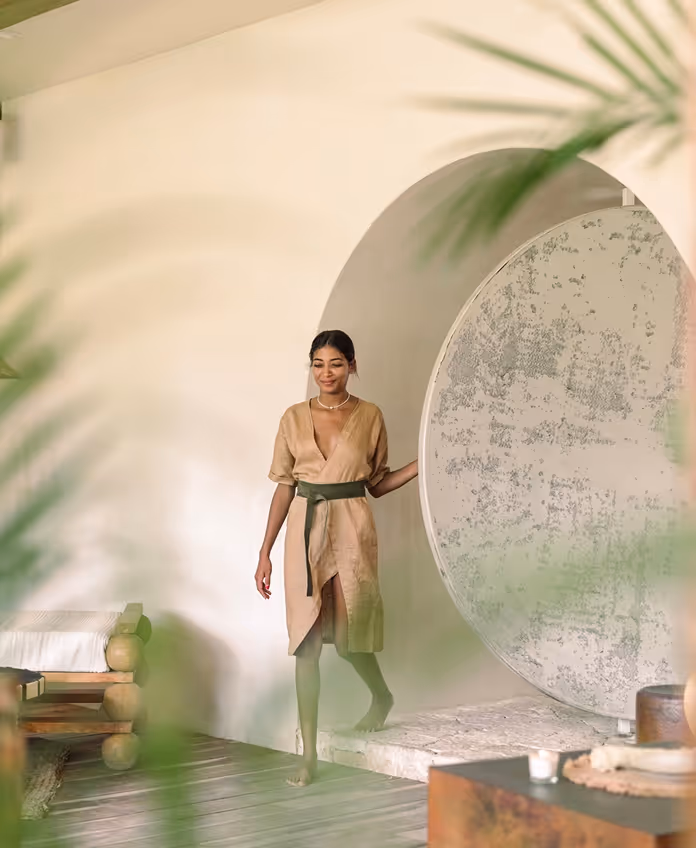 Woman in a linen dress walking through a circular doorway at La Valise Tulum hotel, showcasing minimalist and organic Mexican interior design.