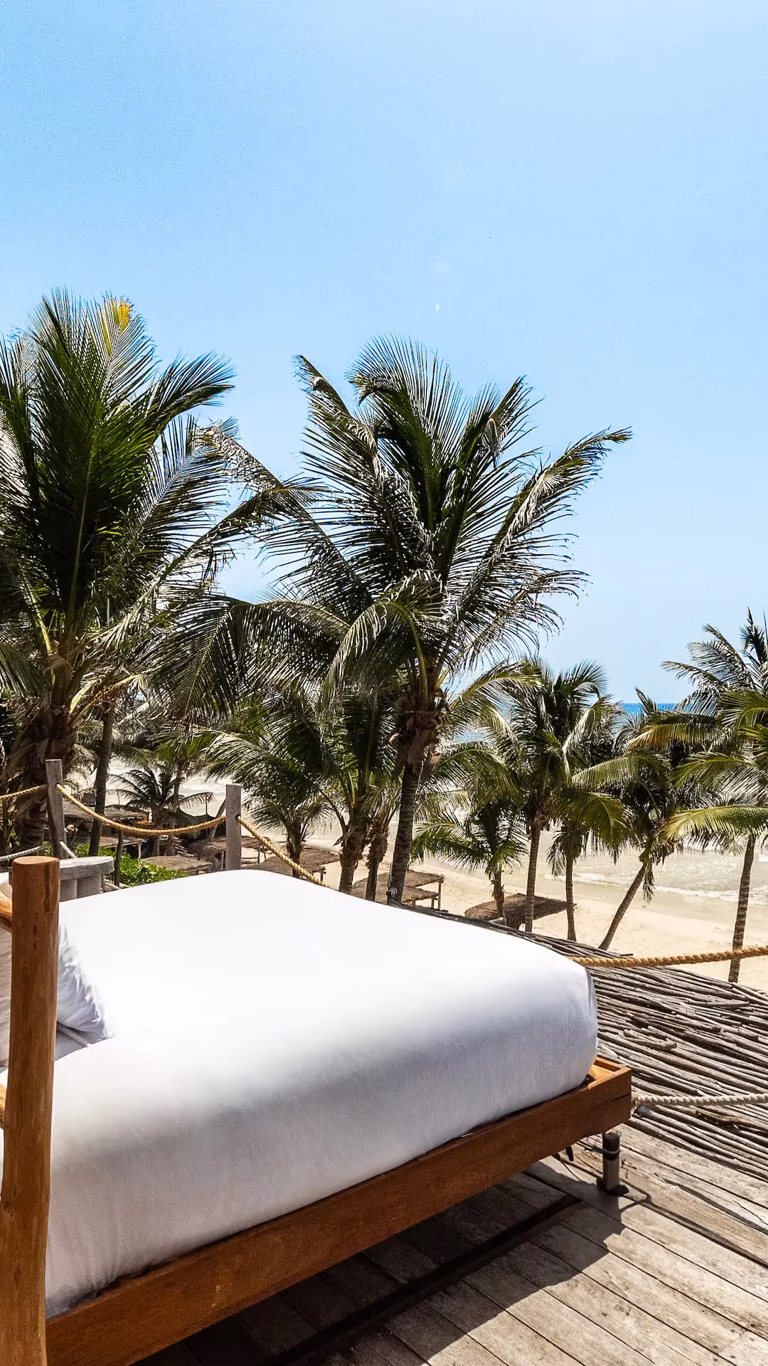 Luxurious outdoor bed on a wooden deck facing palm trees at La Valise Tulum hotel.