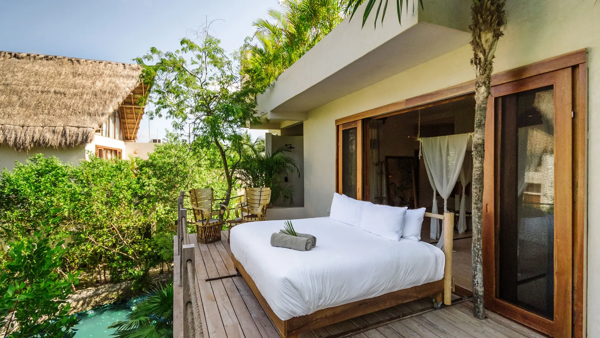 Outdoor bed on a wooden deck at La Valise Tulum hotel, surrounded by tropical jungle greenery.