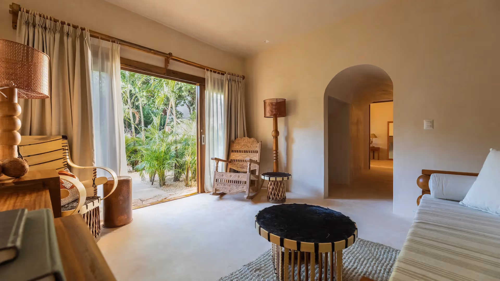 Elegant living area at La Valise Tulum featuring artisanal furniture and a large opening to a lush tropical terrace.