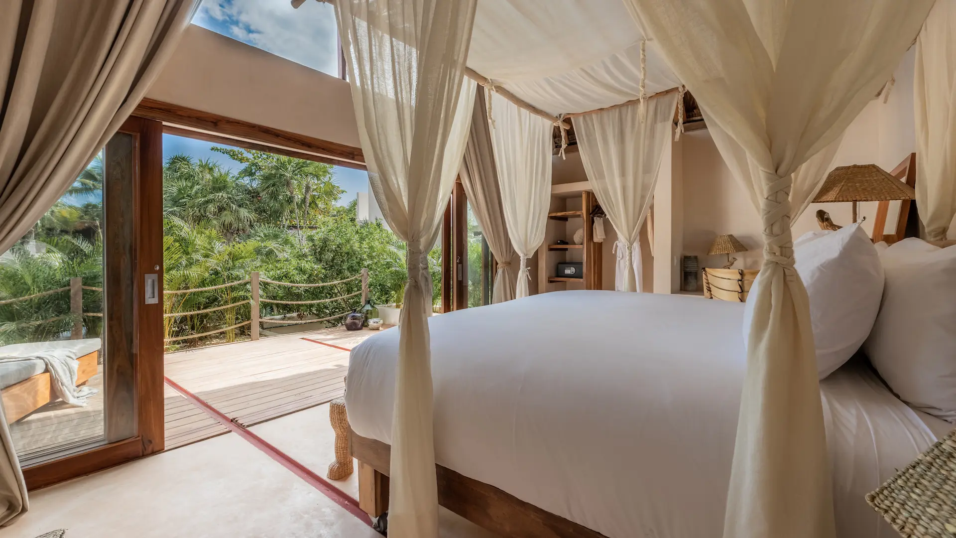 Luxury hotel room at La Valise Tulum featuring a white canopy bed and large glass doors with a scenic jungle view.