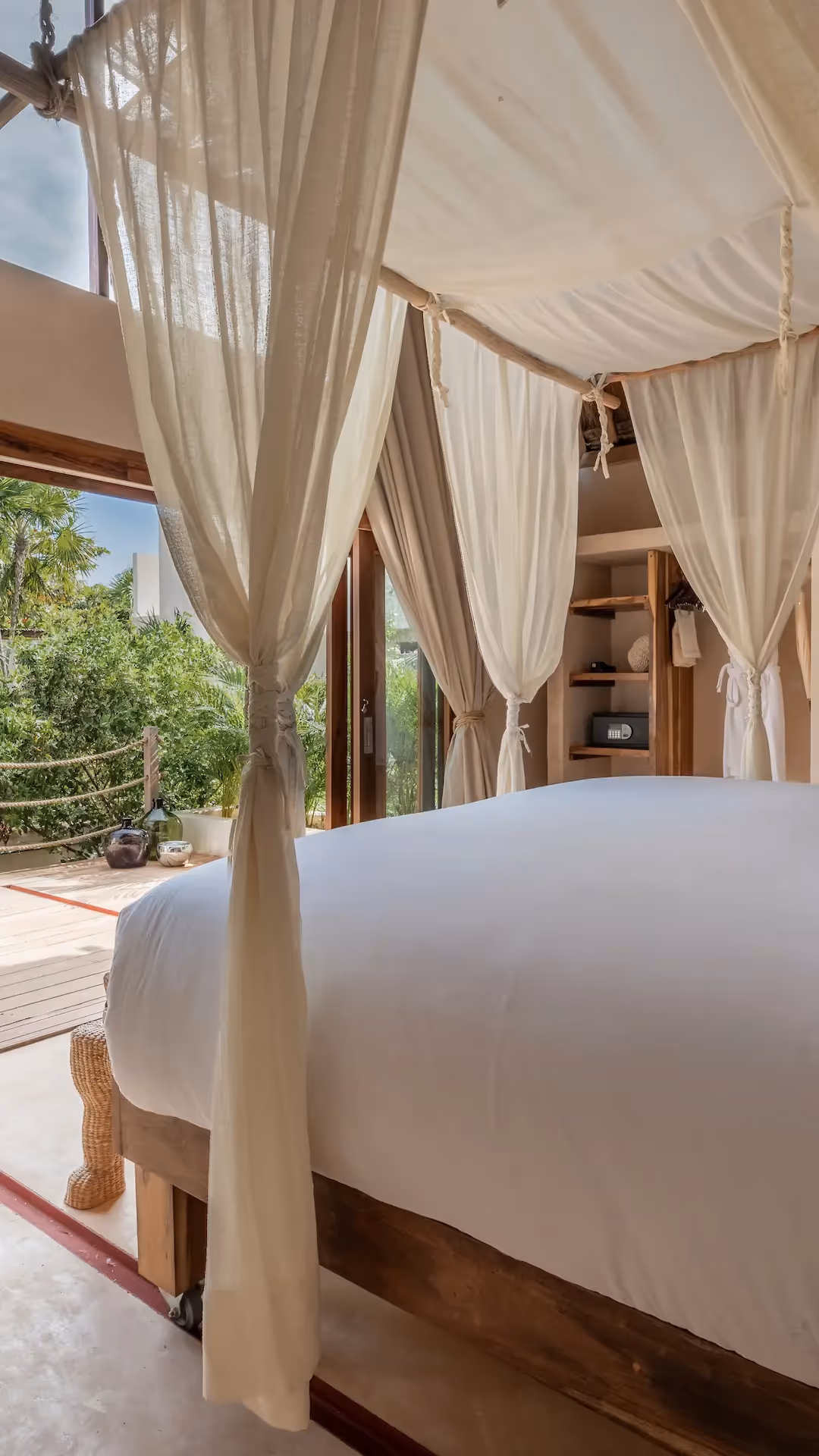 Luxury hotel room at La Valise Tulum featuring a white canopy bed and large glass doors with a scenic jungle view.