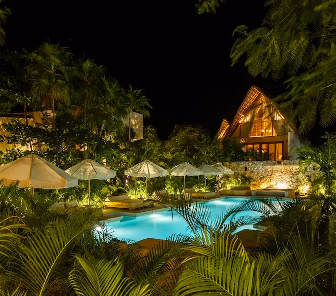 Piscina iluminada y jardines tropicales por la noche en el hotel La Valise Tulum.