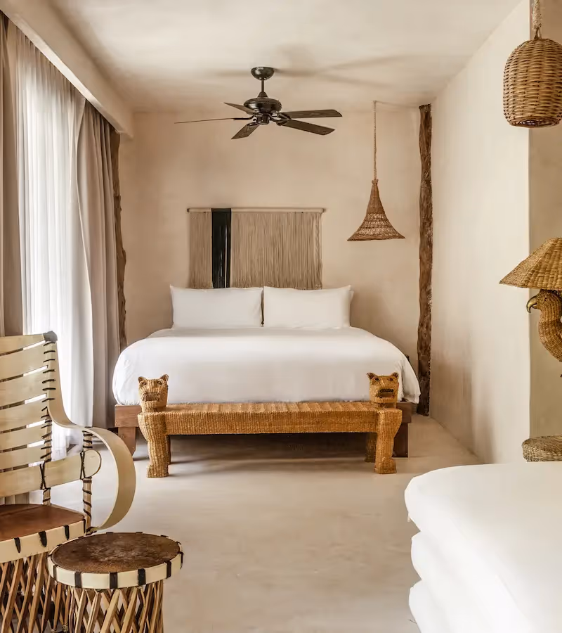 Elegant suite with a king-size bed, woven armchair, and rattan lighting at La Valise Tulum.
