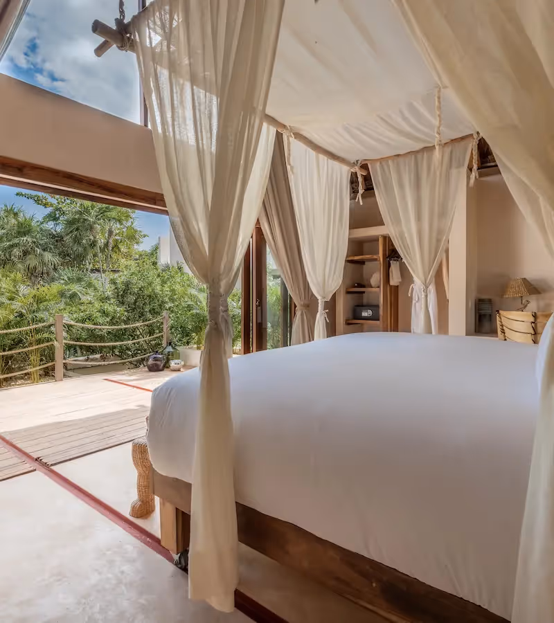 Luxury hotel room at La Valise Tulum featuring a white canopy bed and large glass doors with a scenic jungle view.