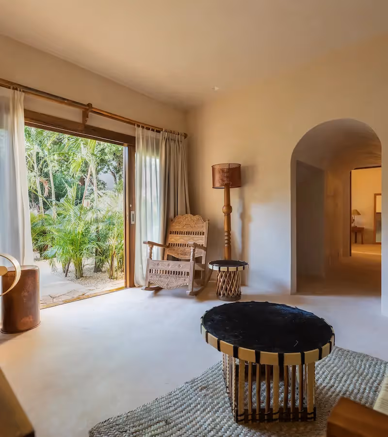 Elegant living area at La Valise Tulum featuring artisanal furniture and a large opening to a lush tropical terrace.