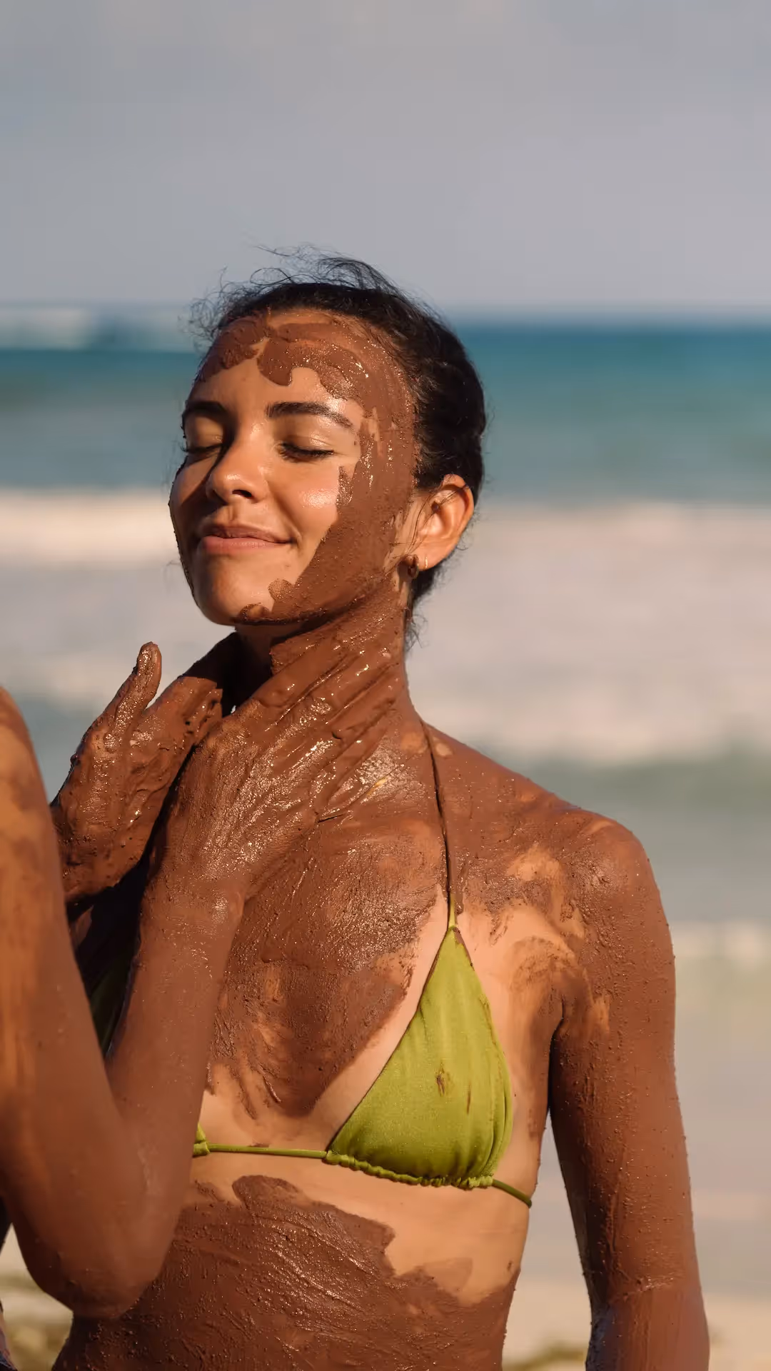 Woman enjoying a traditional Mayan clay skin treatment on the beach at La Valise Tulum hotel.