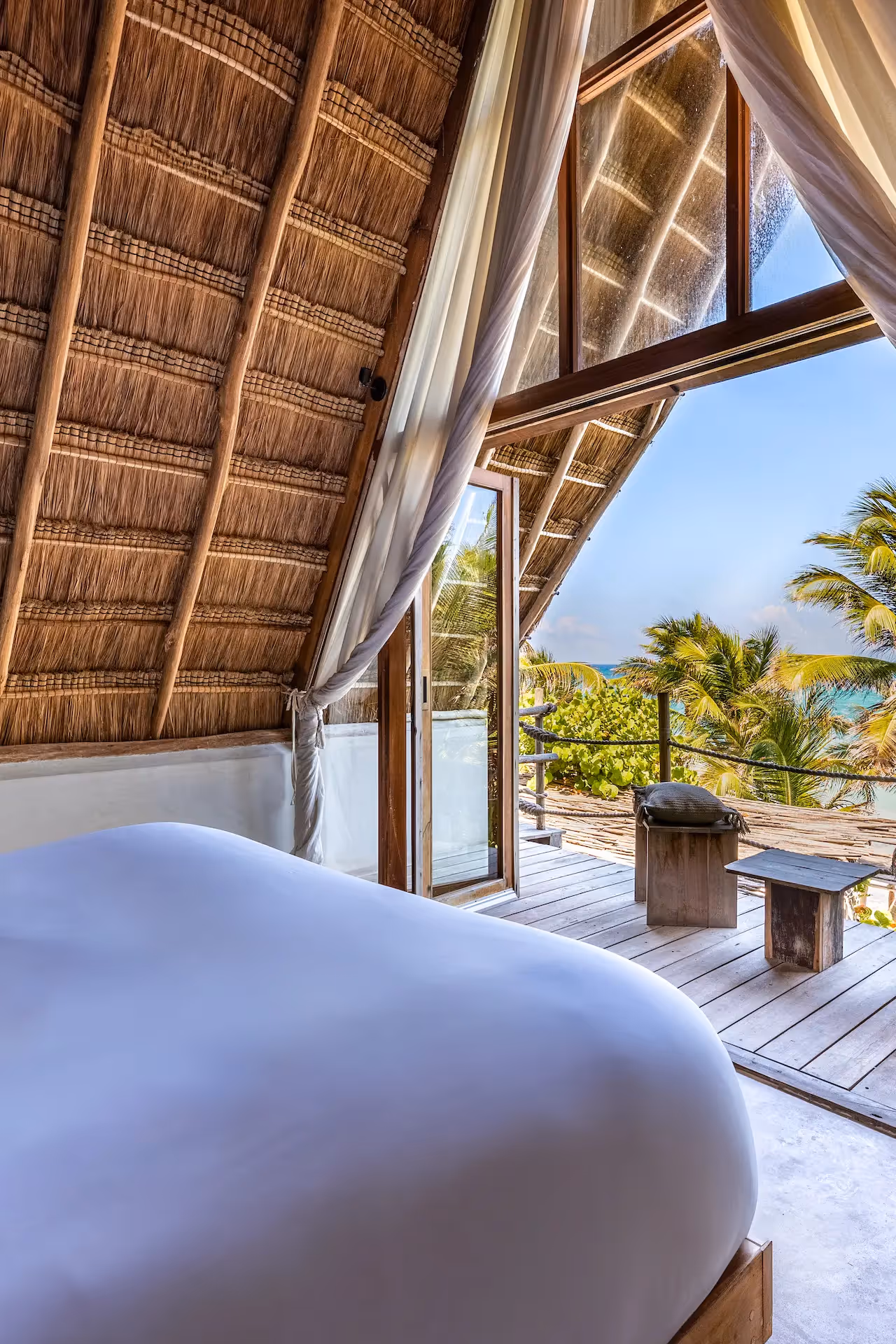 Luxury beachfront suite at La Valise Tulum featuring a canopy bed and floor-to-ceiling windows with private ocean deck.
