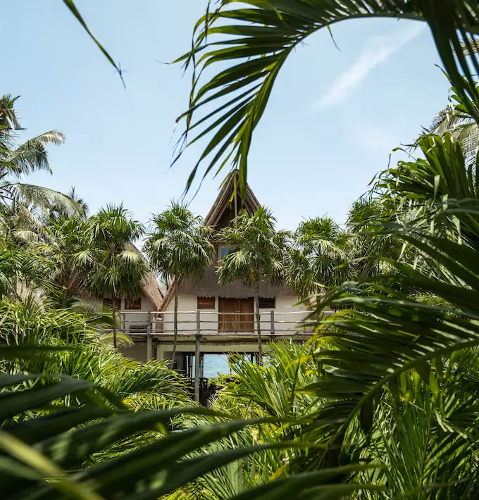 Tropical architecture and traditional thatched roof of La Valise Tulum Hotel surrounded by palm trees.