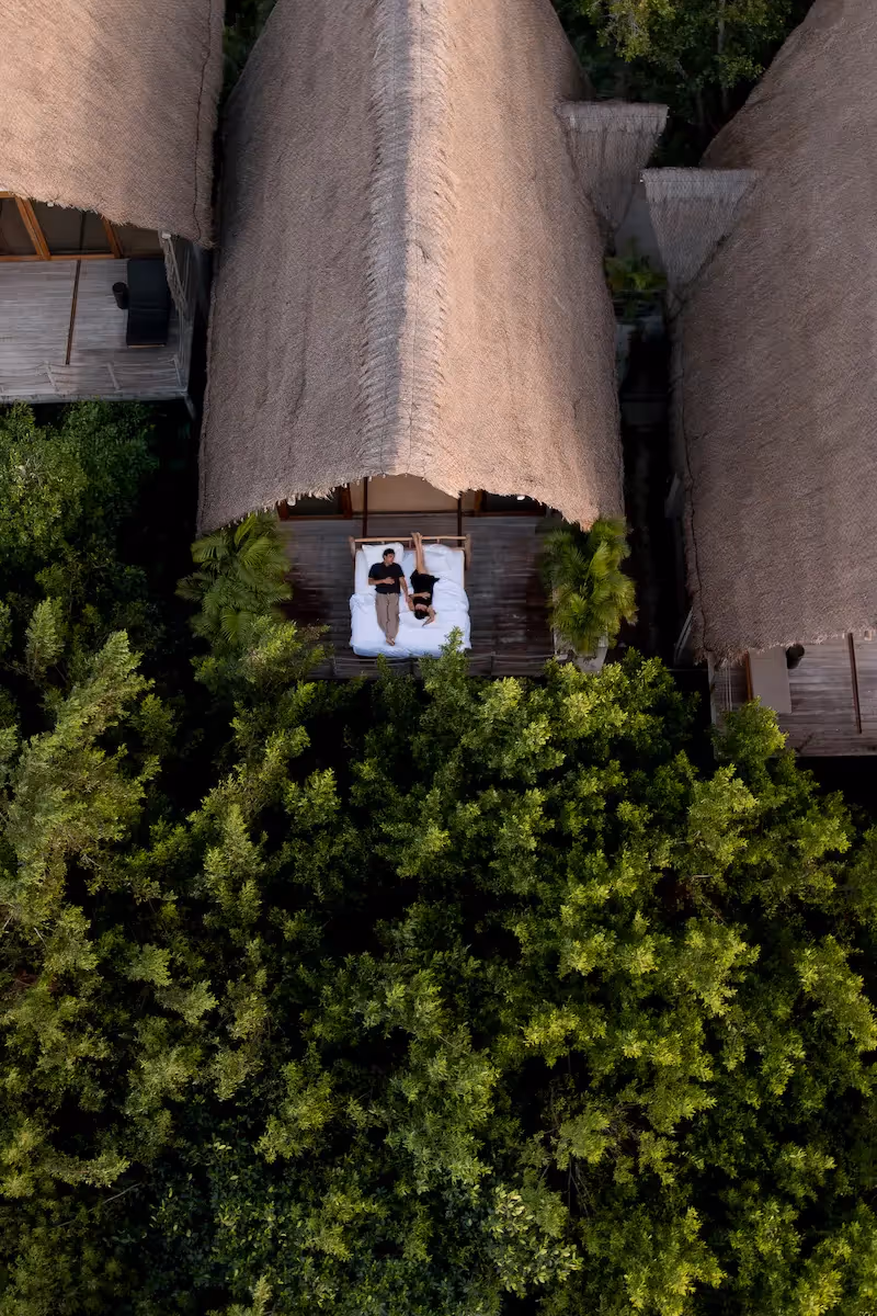 Luxurious outdoor bed on a wooden deck facing palm trees at La Valise Tulum hotel.