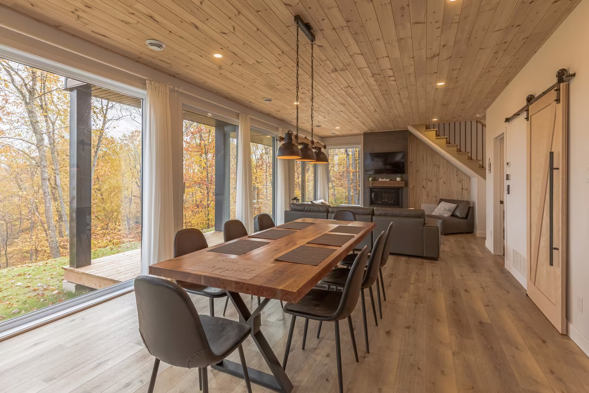 Aire ouverte du chalet LIV Tremblant avec table à manger et grandes fenêtres sur la forêt