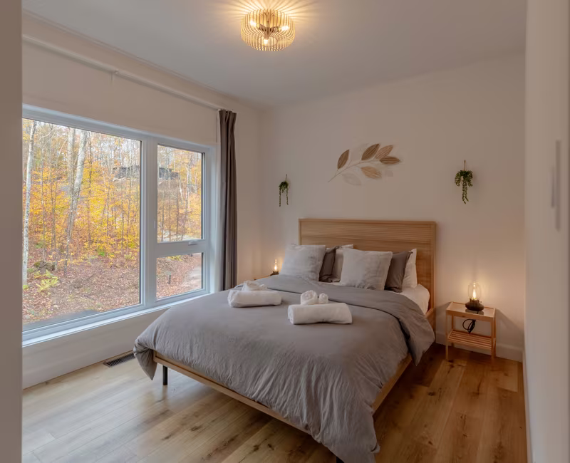 Chambre 4 du chalet LIV Tremblant, grand lit et fenêtre sur les arbres en automne