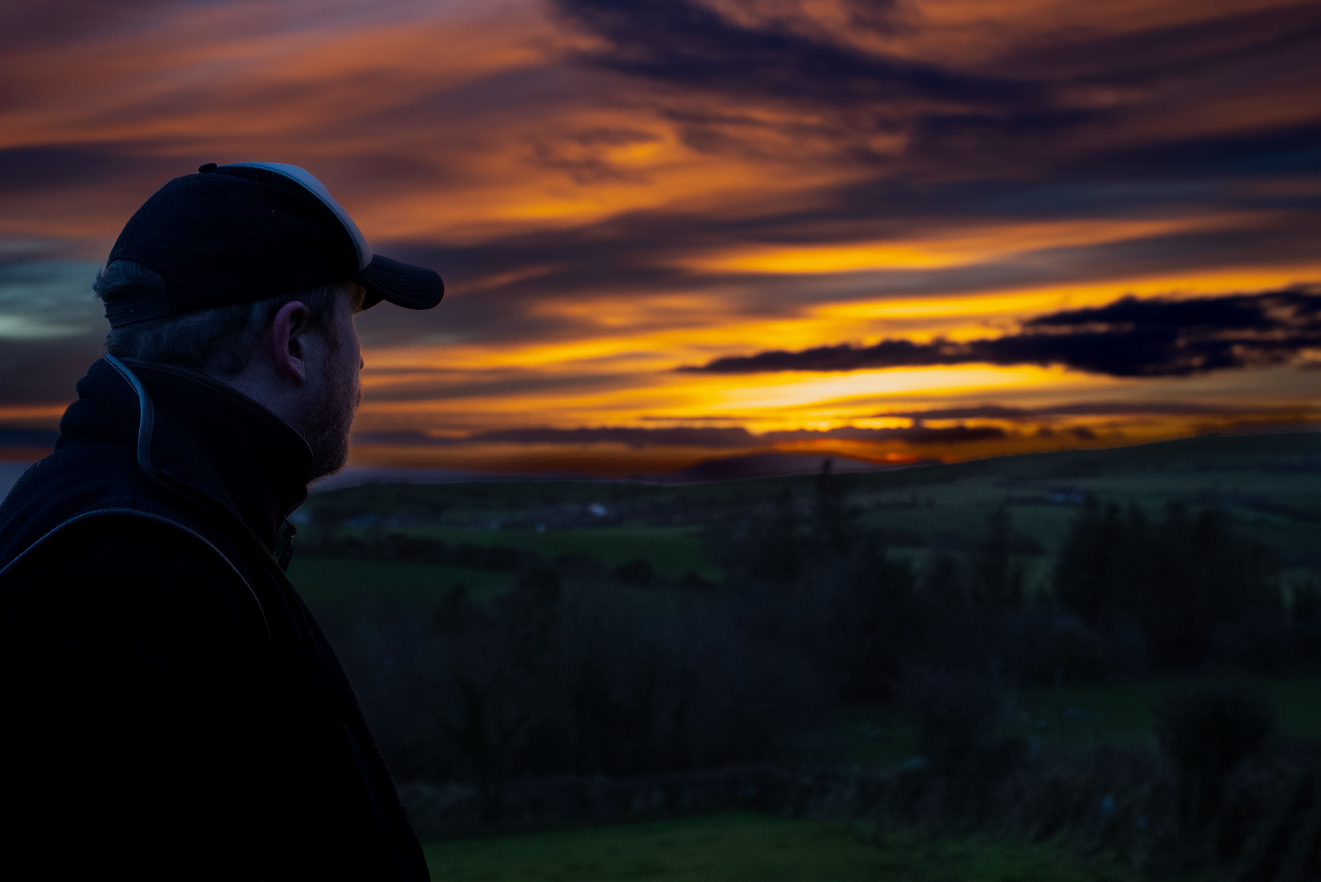 Smiling woman with blonde hair wearing a dark gray hoodie, sitting indoors with green plants in the background.