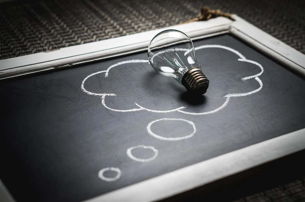 Chalkboard featuring drawing of thought bubble with physical lightbulb placed in middle