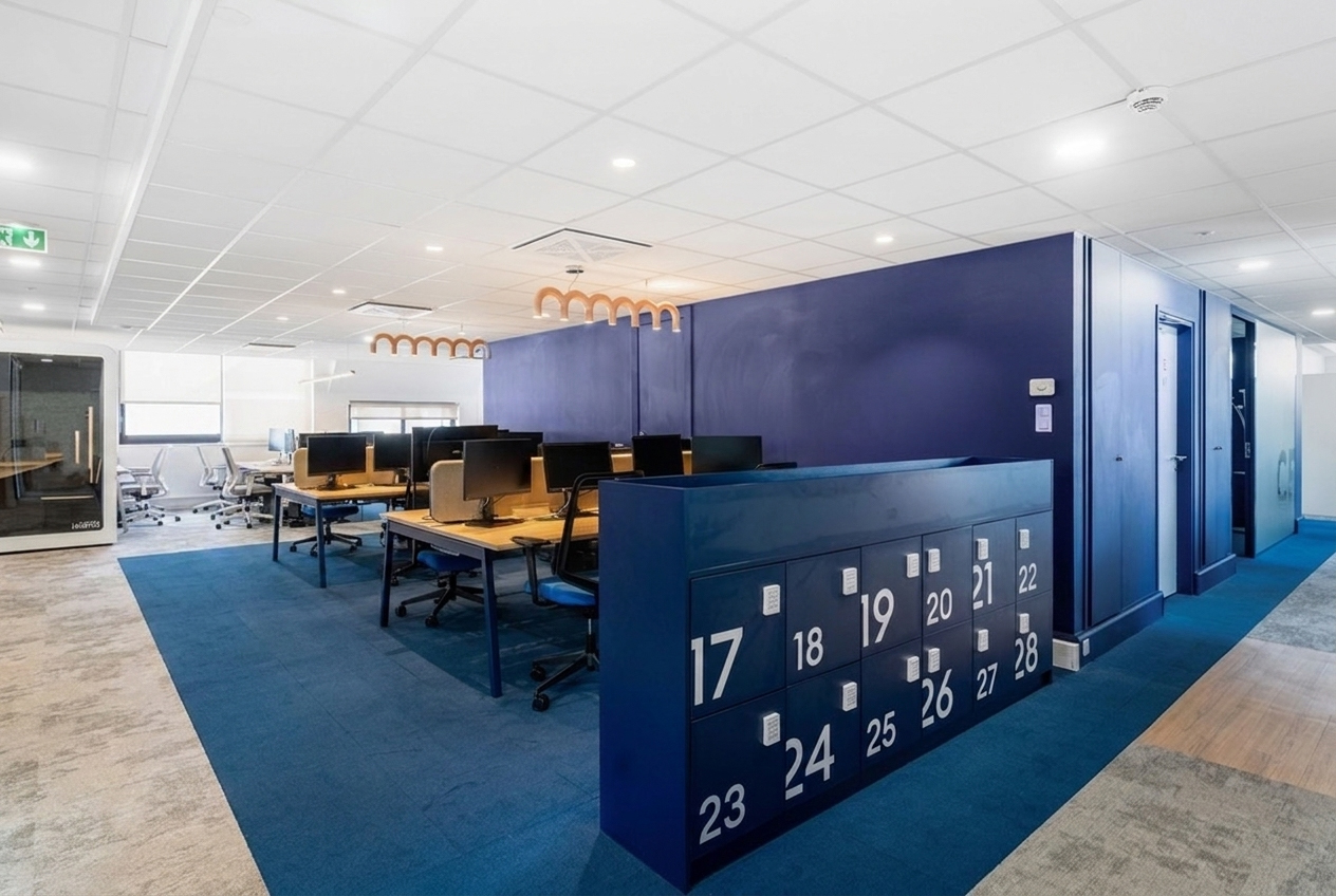 des opens spaces avec des bureaux et des chaises, des salles de réunion avec des télévision pour projeter, des murs blancs et une moquette gris claire ou bleu, des casiers 