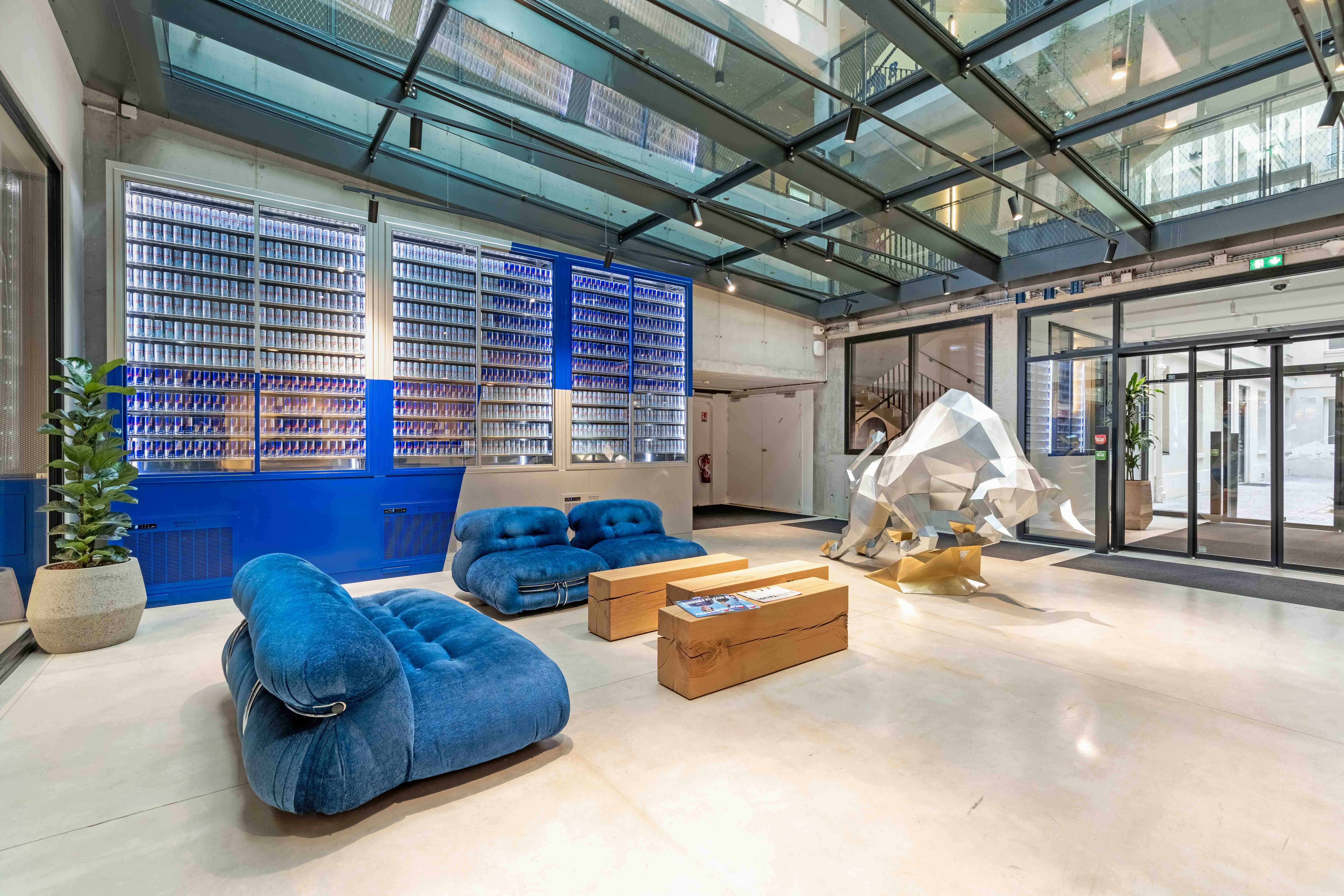 un rand open space sol gris et mur blanc avec des chaises et des bureaux. 2 salles de réunion avec des chaises et une table et un écran. un espace détente avec un canapé et une table de salle a manger. des phone boxes avec des chaises