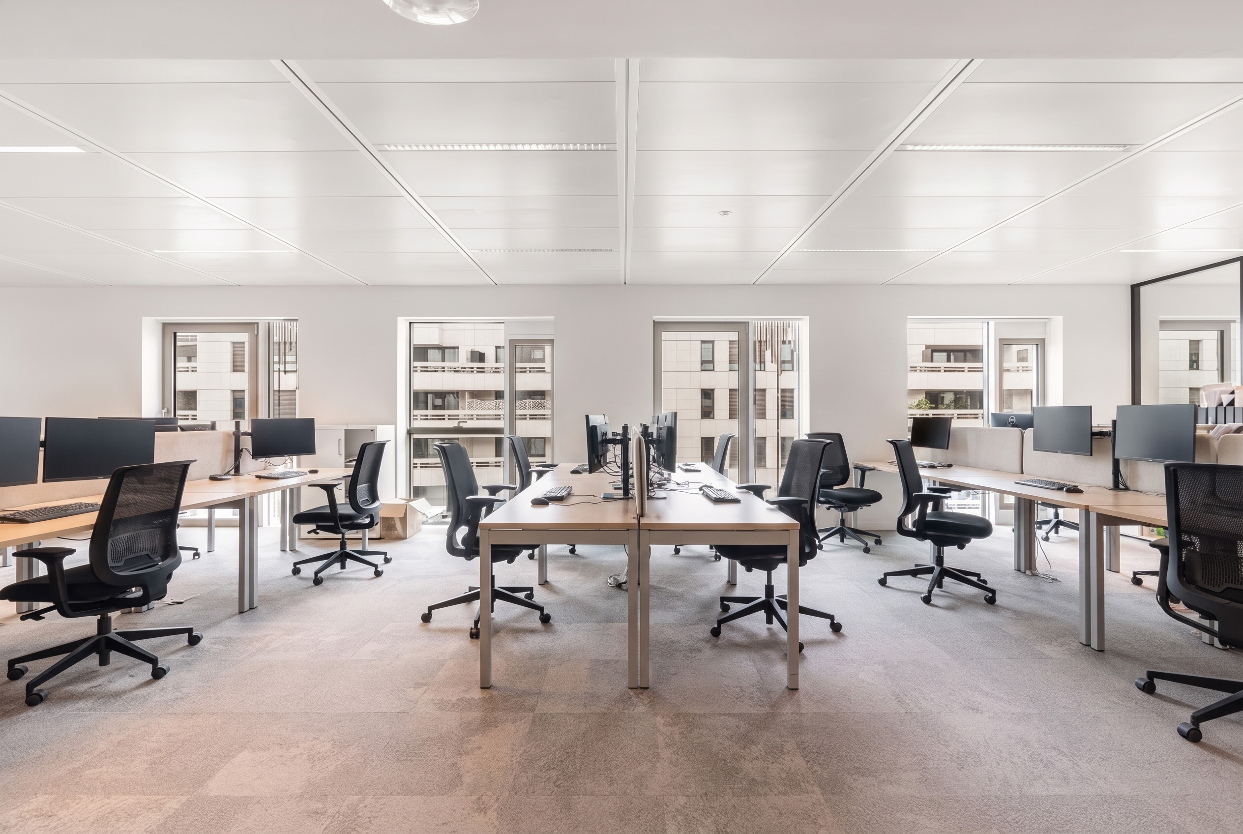 des bureaux et des chaises dans un open space avec de la moquette claire et des mur blancs. des salles de réunion avec des tables et des chaises. une cuisine équipée avec des tables hautes et des chaises hautes. 