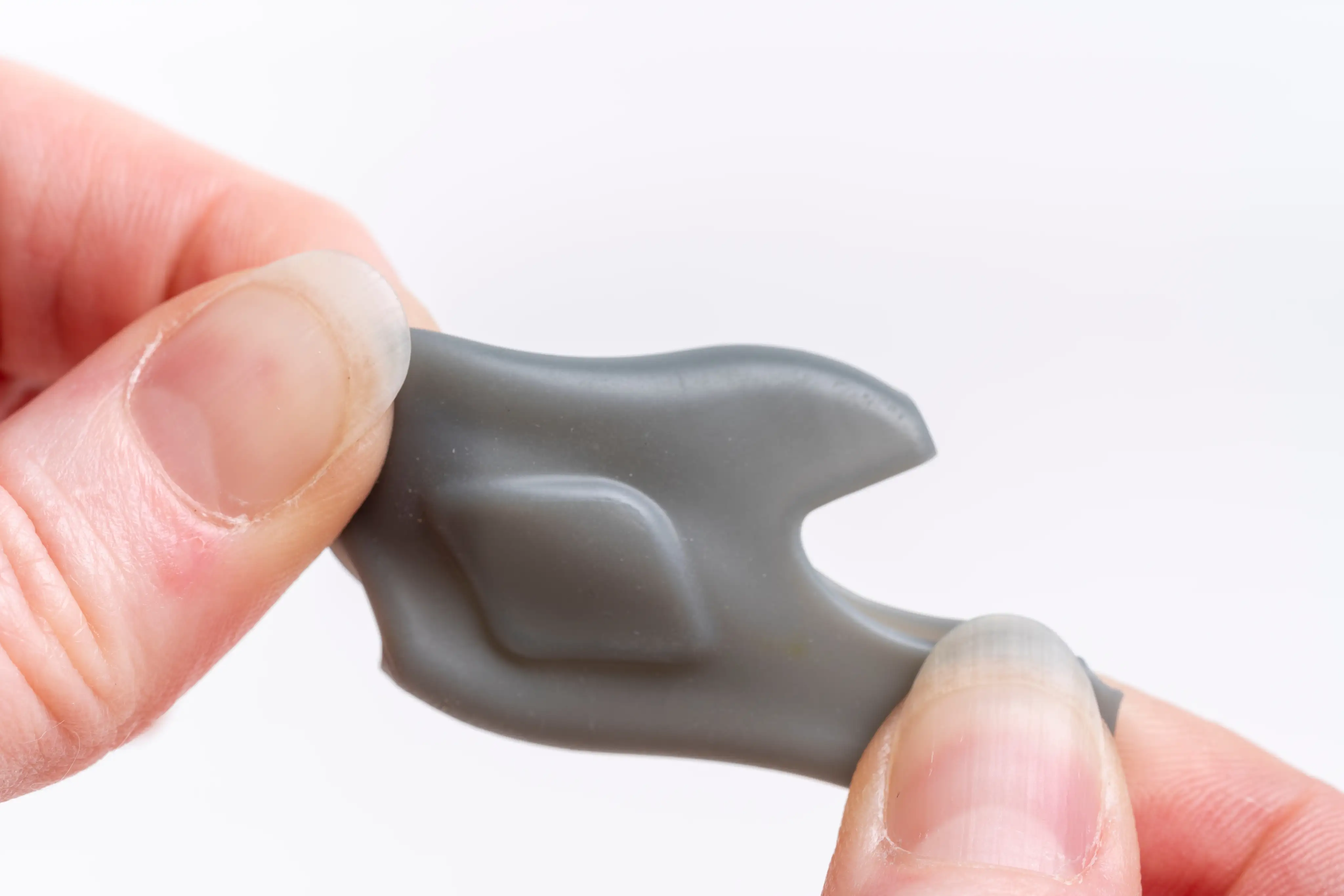 Close-up of hands holding a small flexible gray plastic piece with a raised diamond shape.