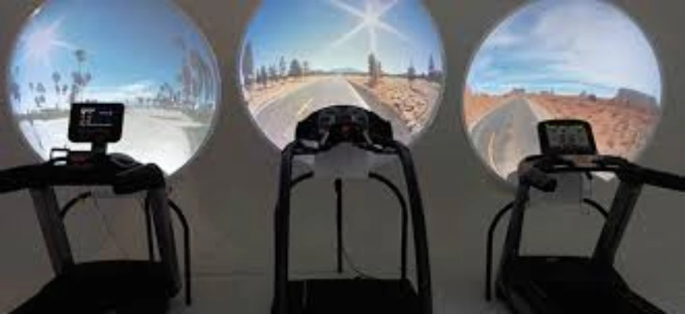 Three treadmills positioned in front of circular screens showing outdoor road scenes with sunny skies.