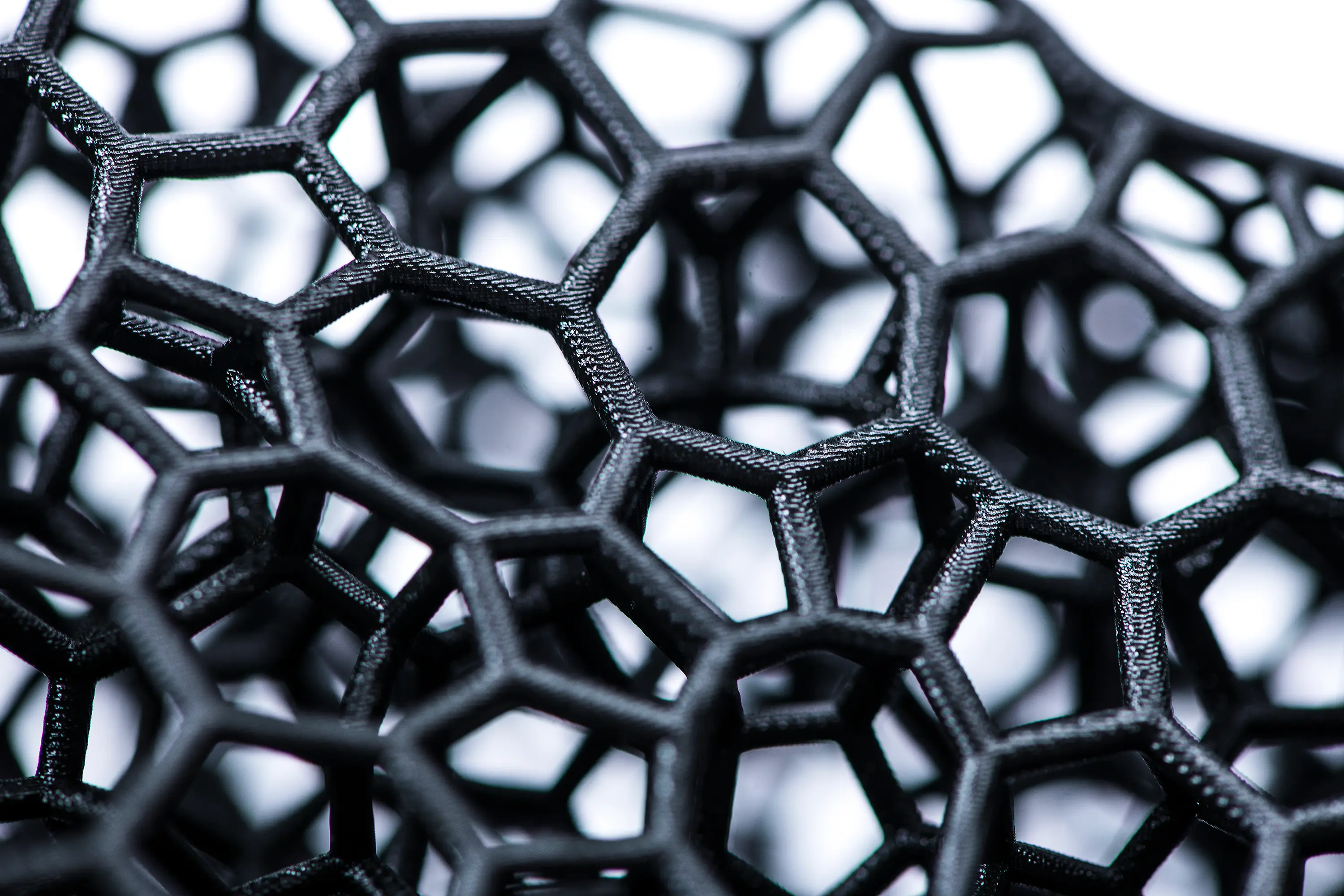 Close-up of black, hexagonal-patterned mesh structure with high detail and texture made on carbon printer.