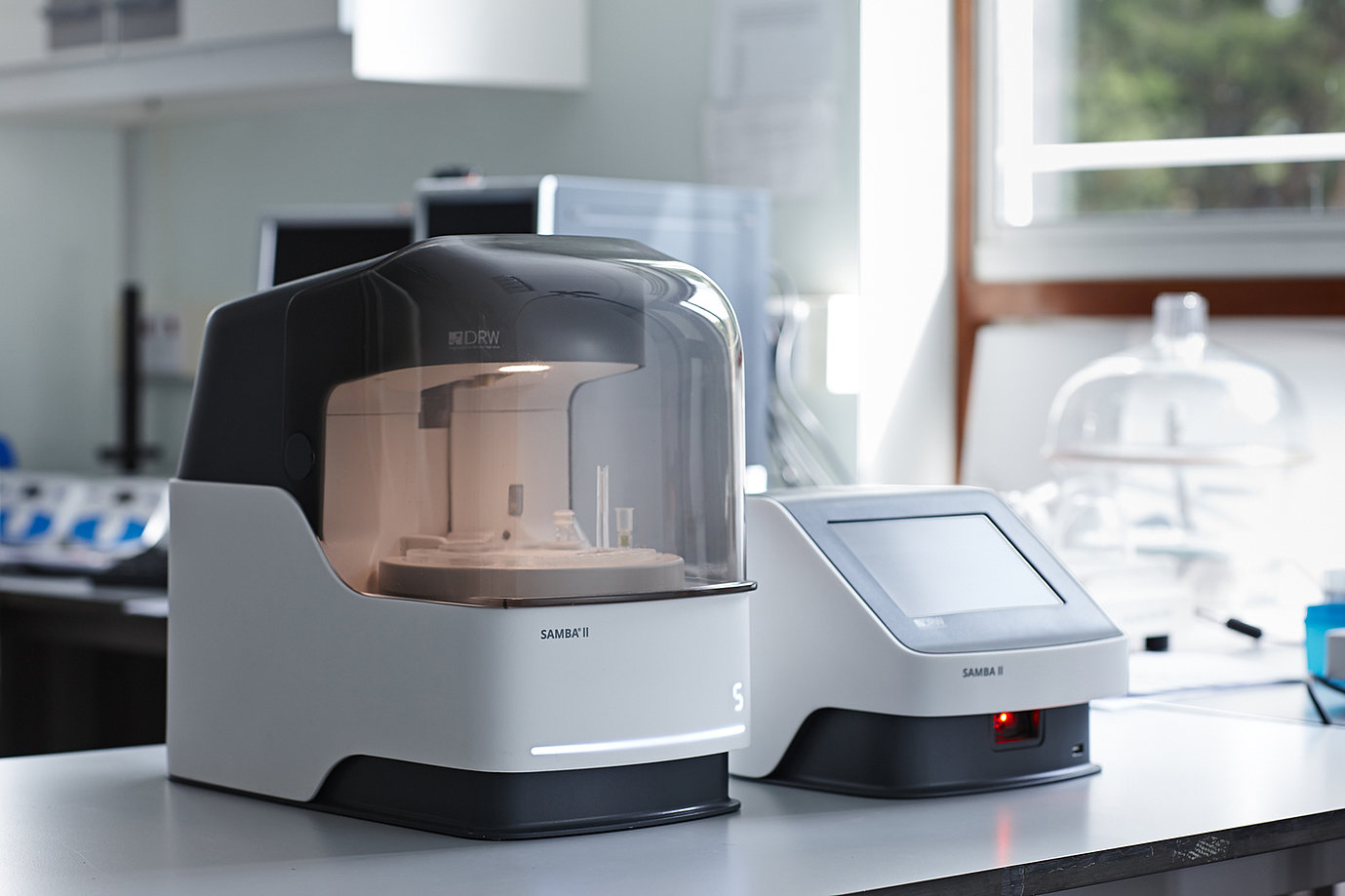 Modern laboratory analyzer device labeled SAMBA II on a white table in a clinical lab setting.