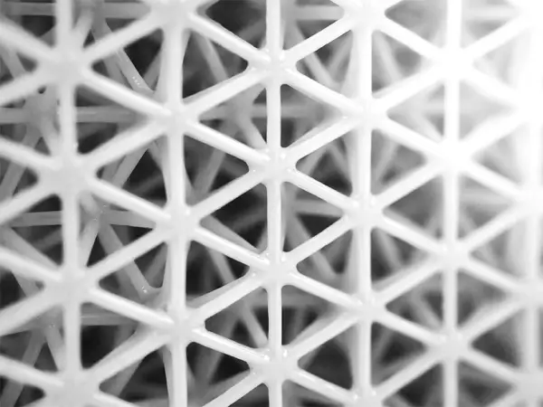 Close-up of a white 3D printed lattice structure with intersecting triangular patterns.