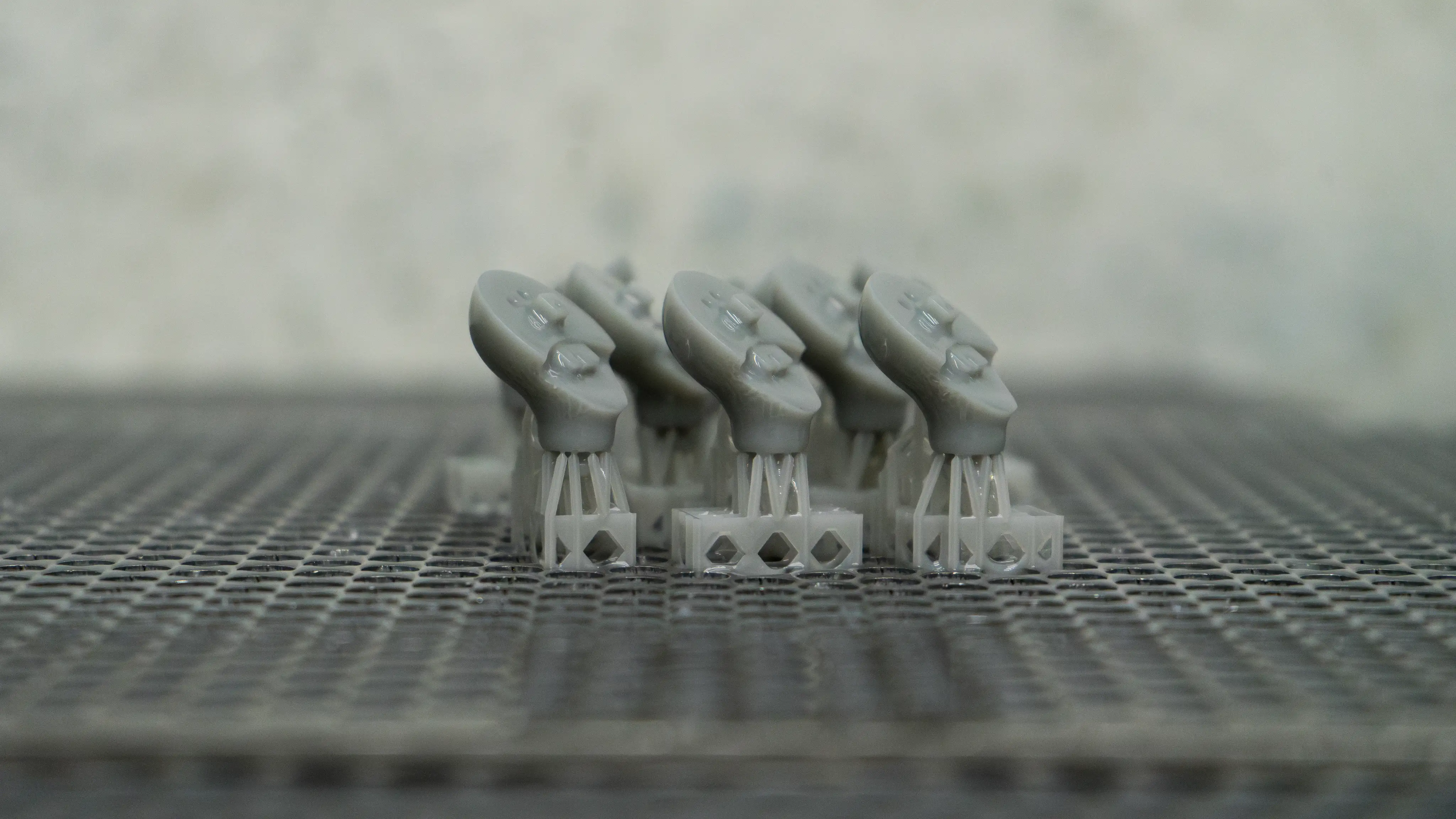 Close-up of gray 3D-printed plastic parts arranged in rows on a perforated surface.
