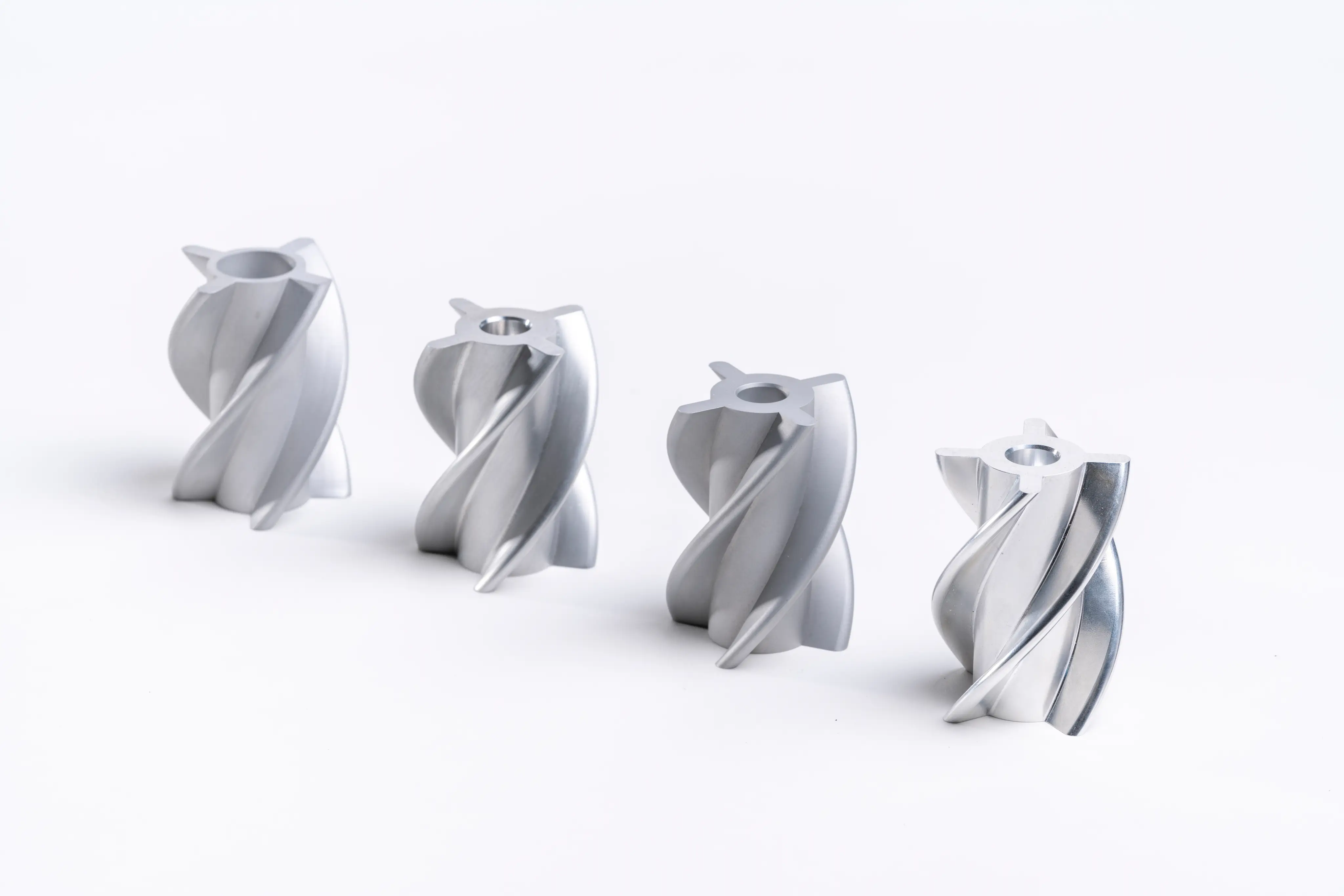 Four silver metal impeller blades arranged in a row on a white surface.