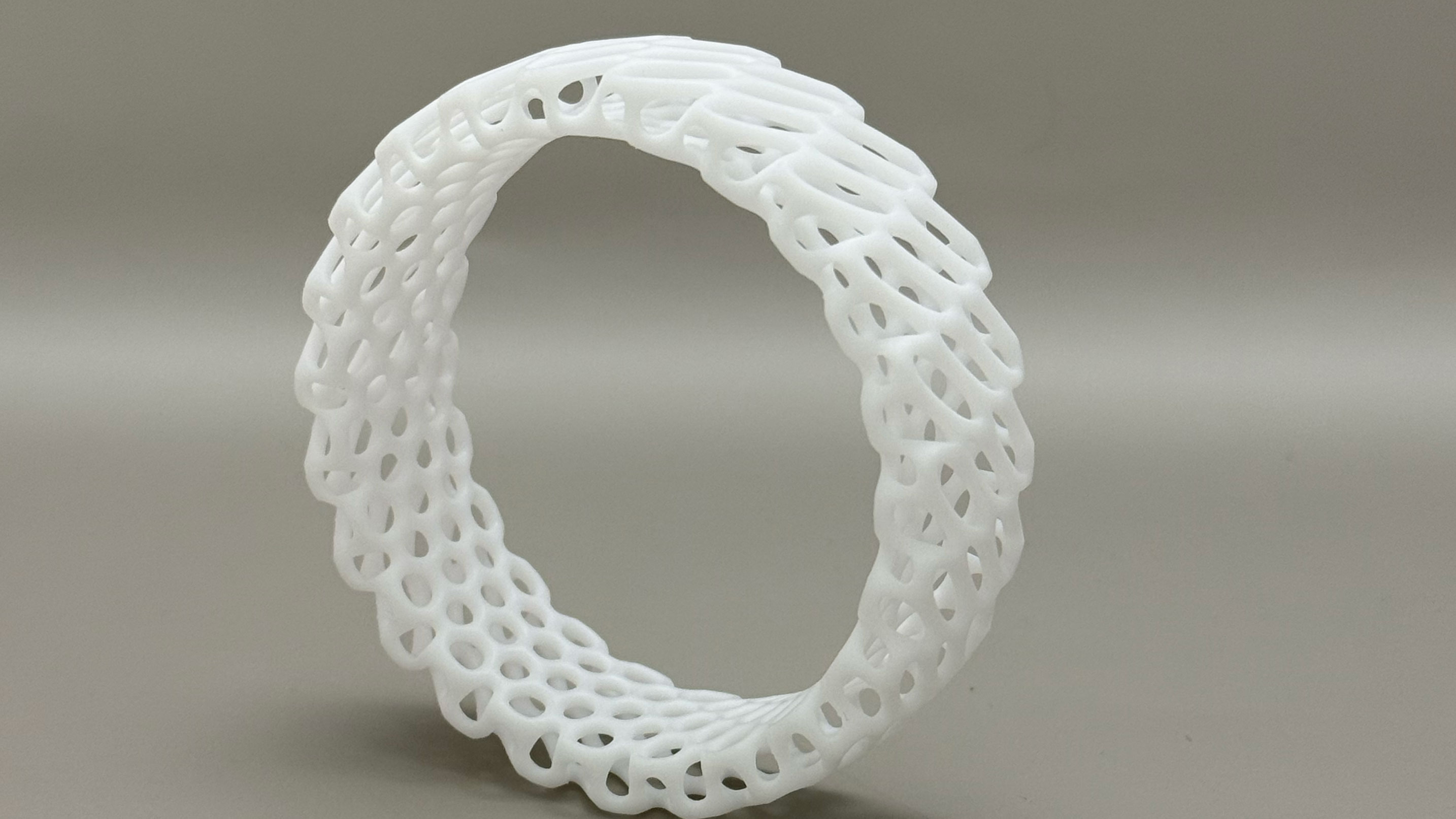 White 3D-printed ring with an intricate lattice structure on a plain background.