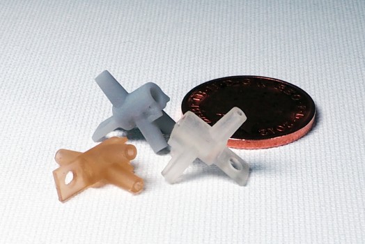 Three small vacuum-cast polyurethane components in grey, clear and amber beside a coin for scale