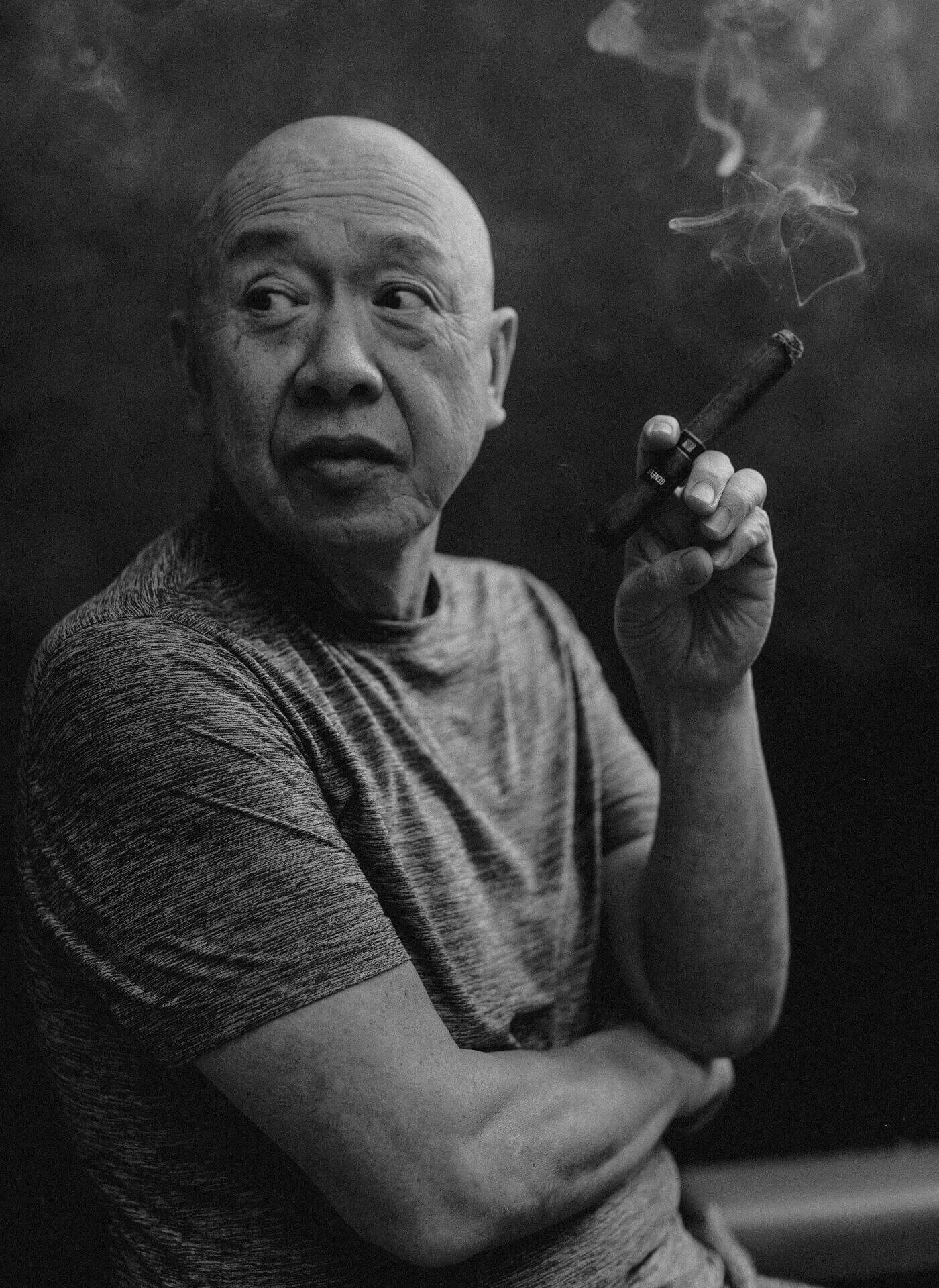 A monotone image of Chef Masa smoking a cigar