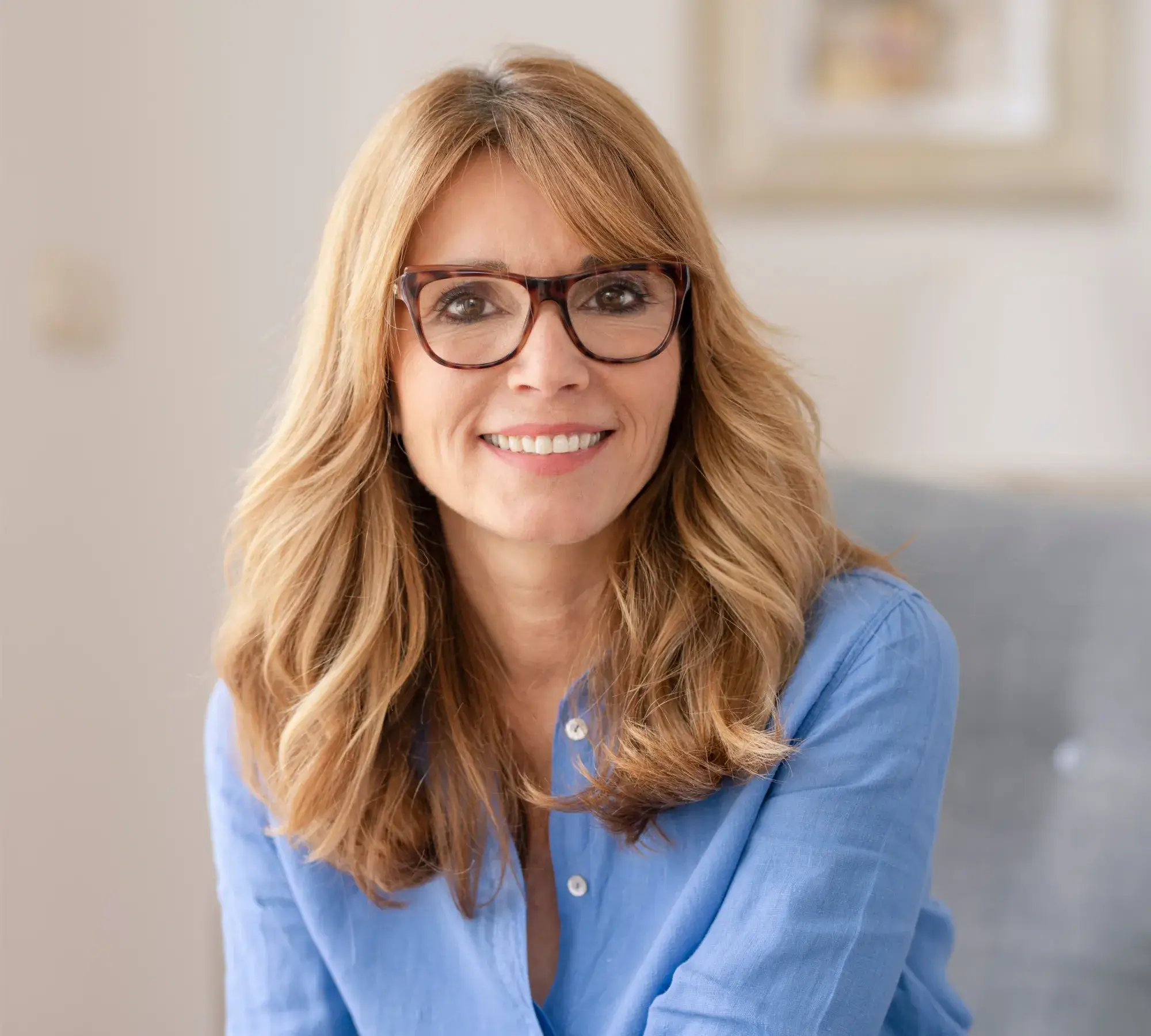 Smiling middle-aged woman with glasses and shoulder-length blonde hair wearing a blue shirt.