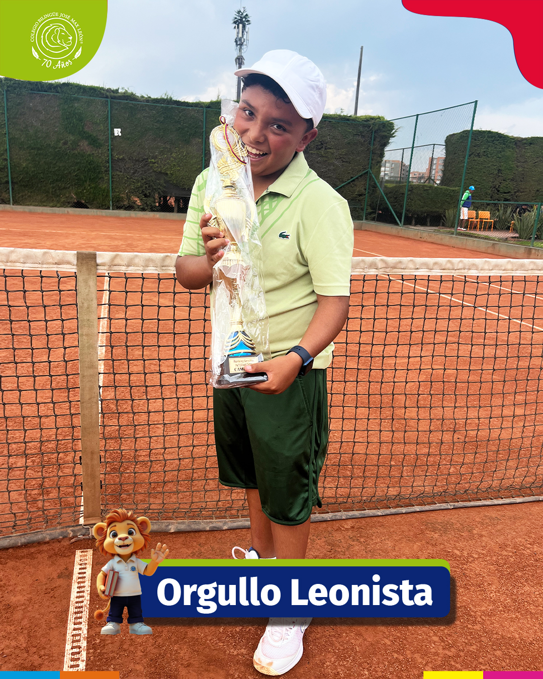 Niño sonriente sosteniendo un trofeo grande en una cancha de tenis de arcilla.