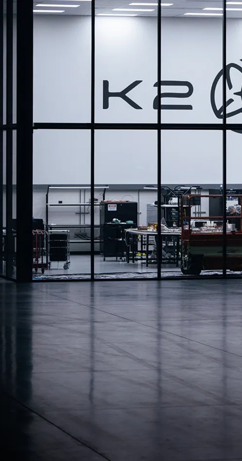 Engineers working inside the K2 Space manufacturing facility, assembling satellite components behind large glass panels