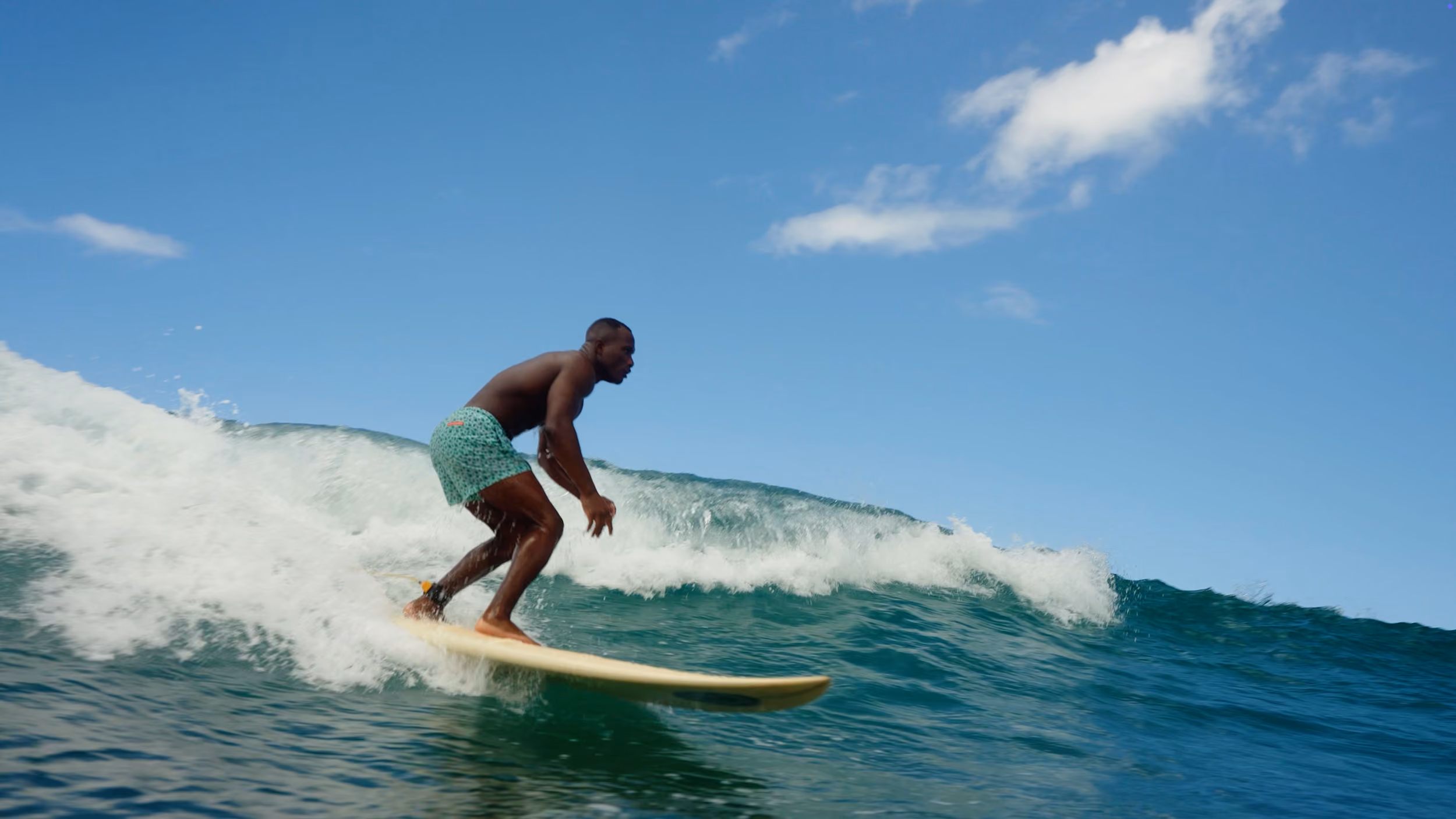 Man surfing on a yellow surfboard riding a wave under a blue sky with scattered clouds.