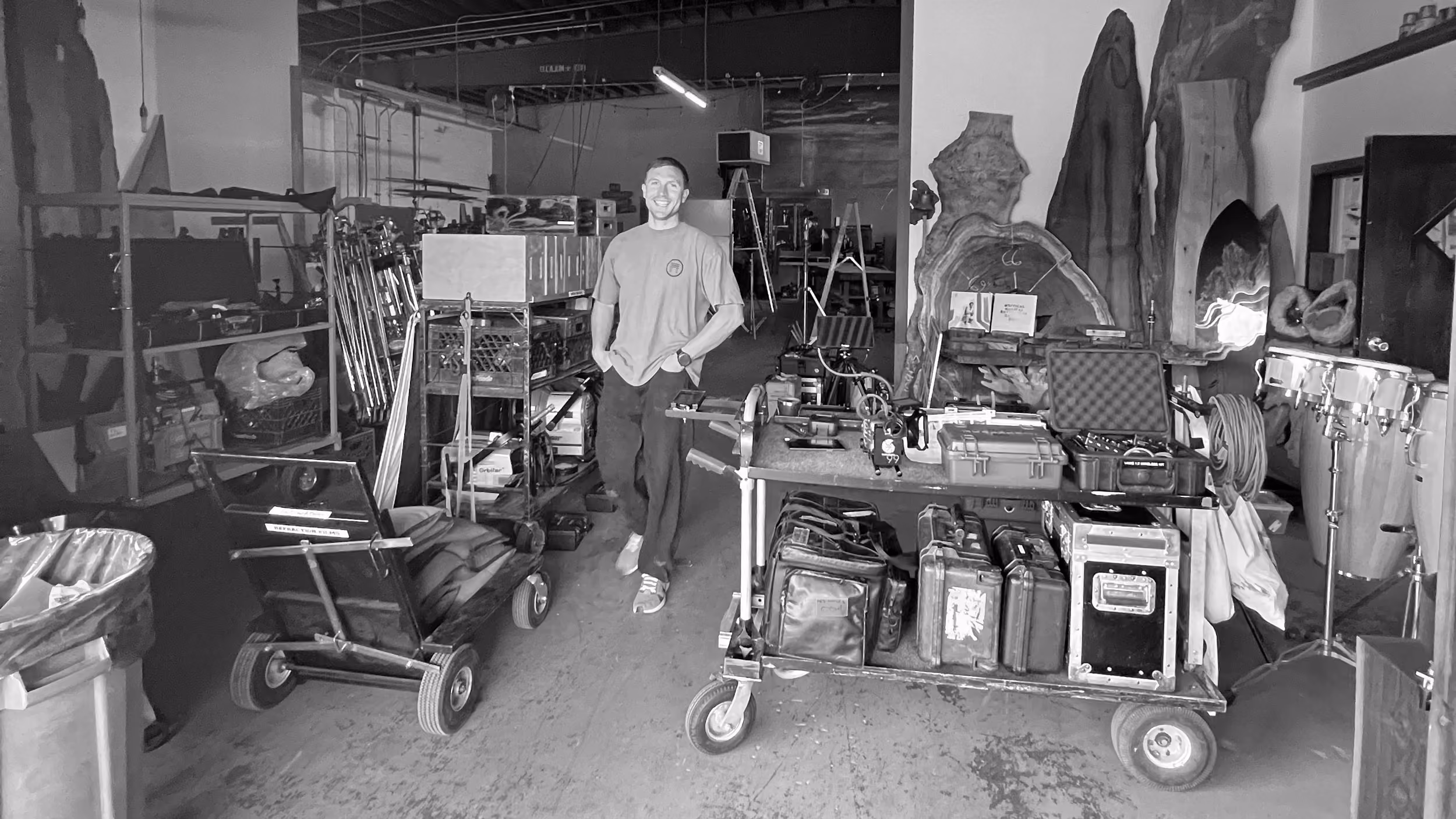 Founder Brett Hoffman standing in a warehouse surrounded by film or photography equipment on carts and shelves.