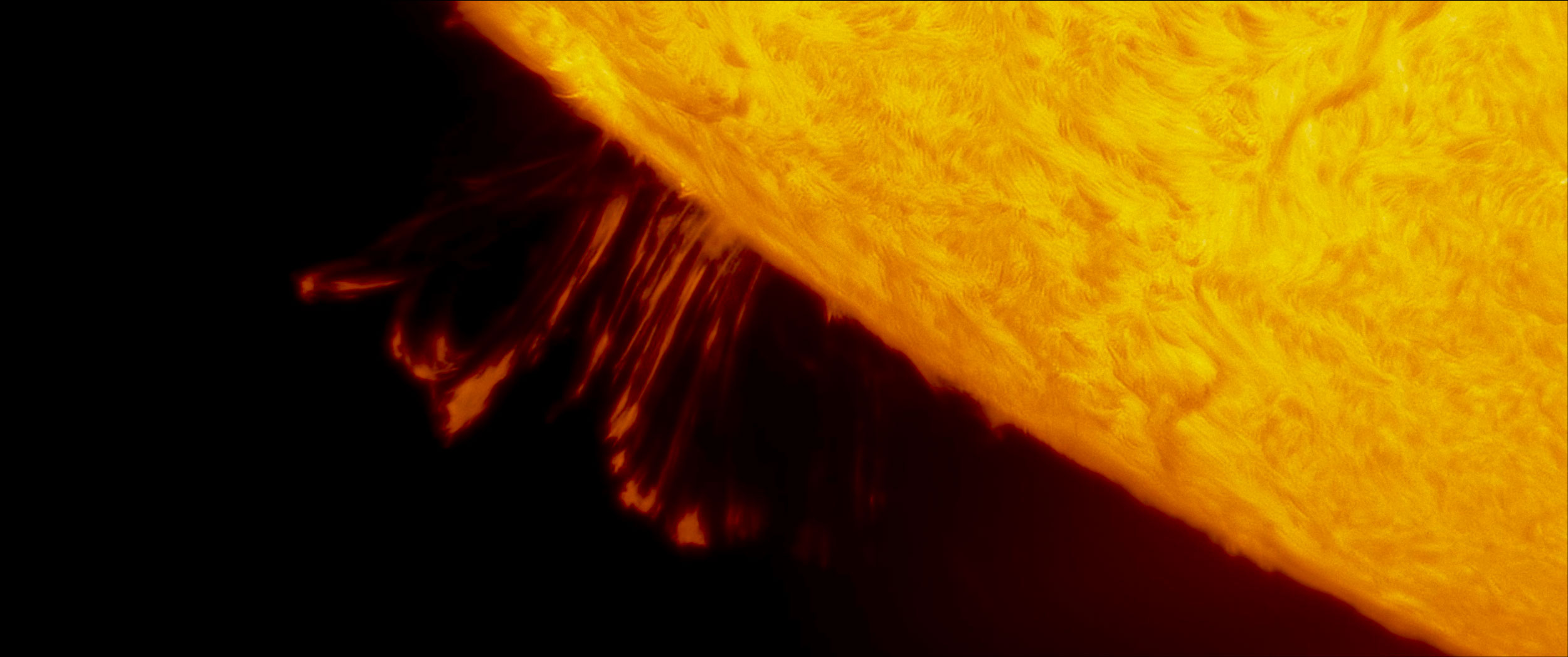 Man in green shirt holding a remote controller in a dimly lit workshop with a wooden workbench and tools on the wall.
