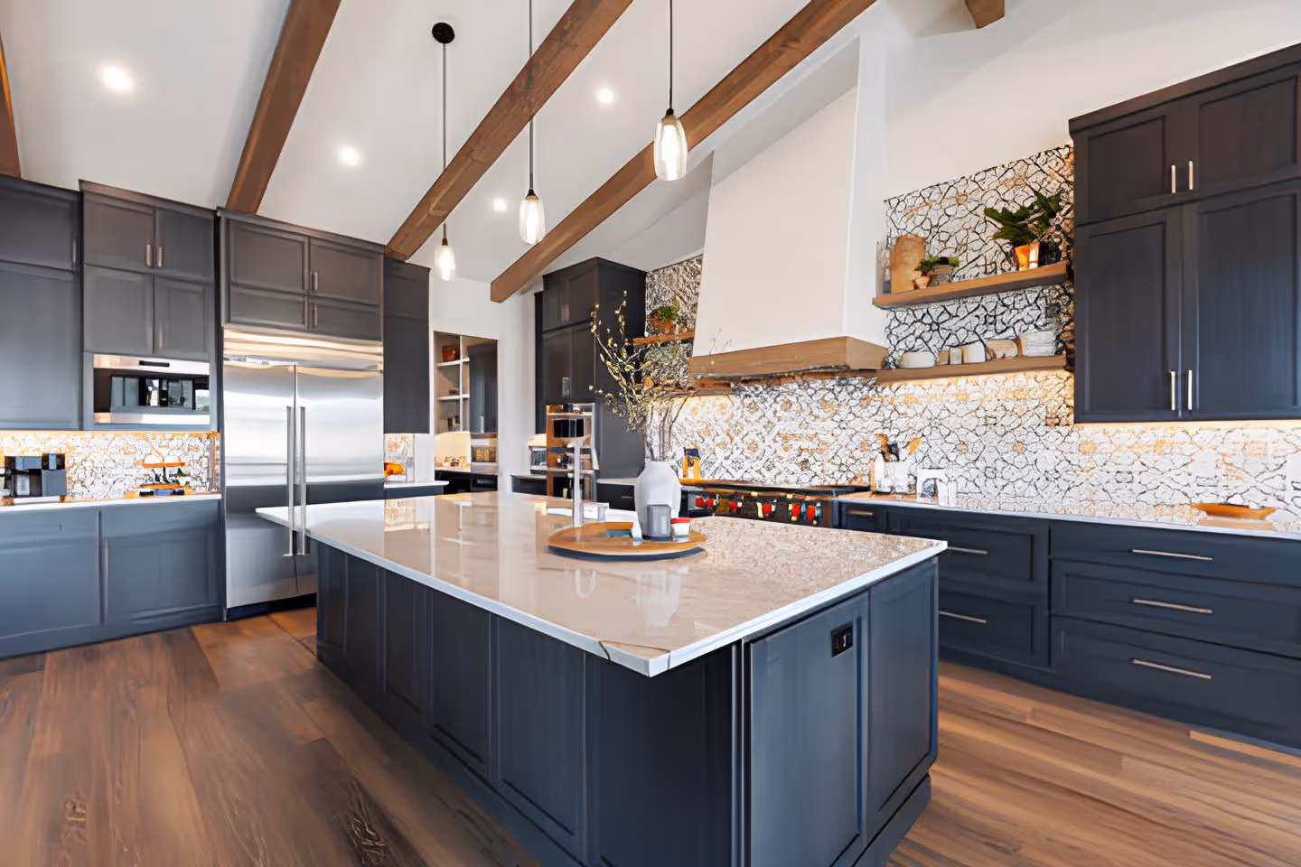 Modern kitchen with dark cabinetry, a large white marble island, wood ceiling beams, and patterned backsplash tiles.