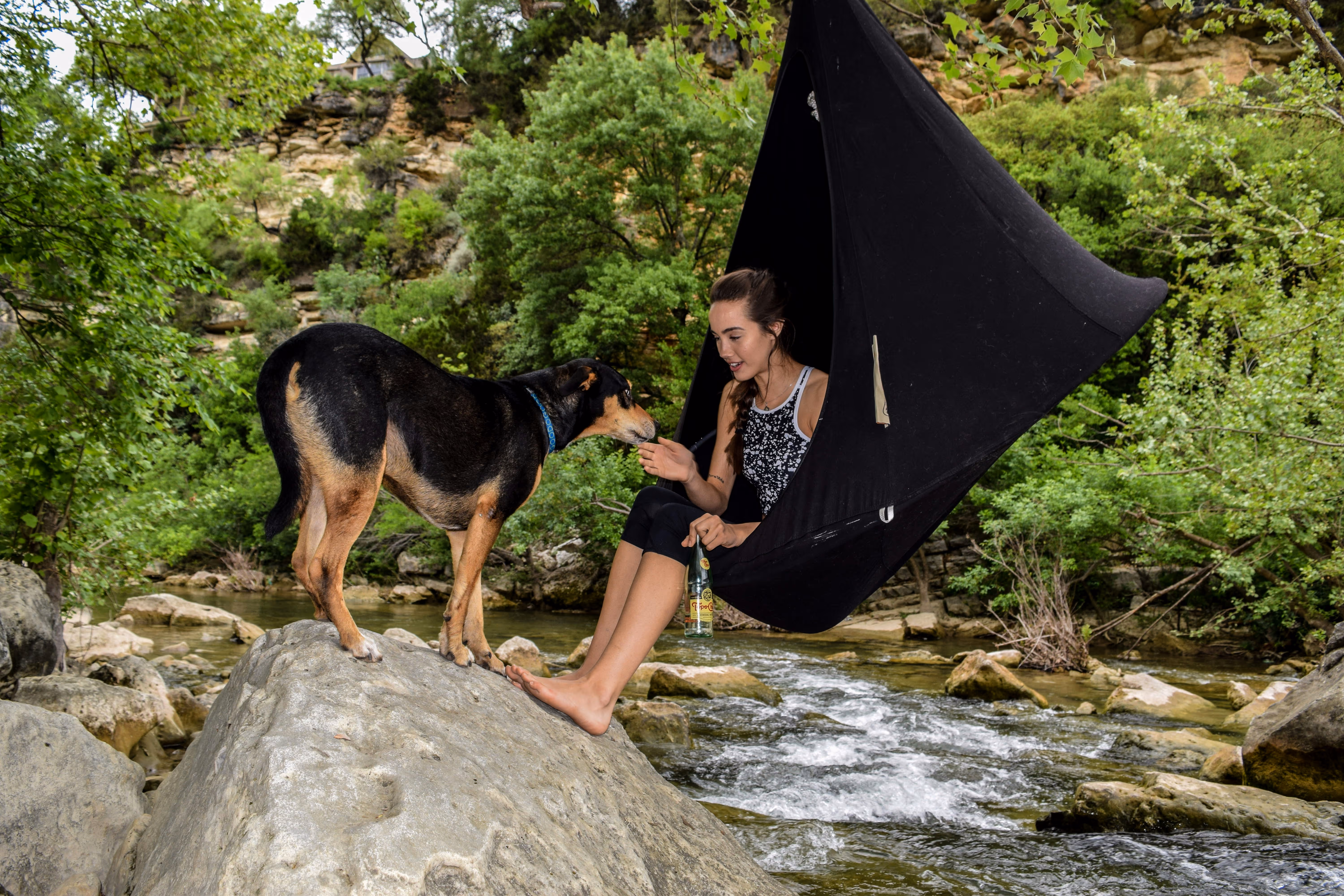 A girl camping outdoors with her German Shepherd as they enjoy time by a creek.