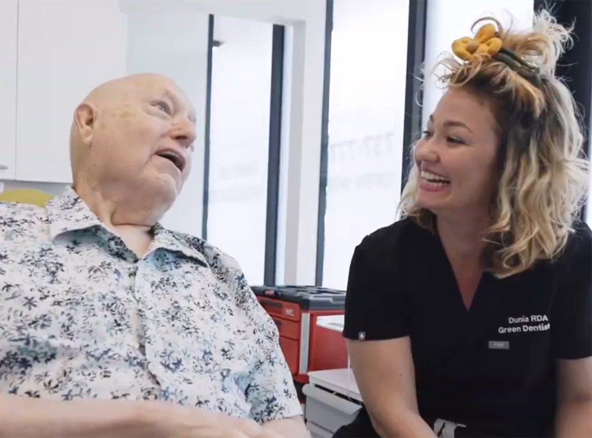 Smiling female dentist interacting with an elderly male patient in a bright dental office.