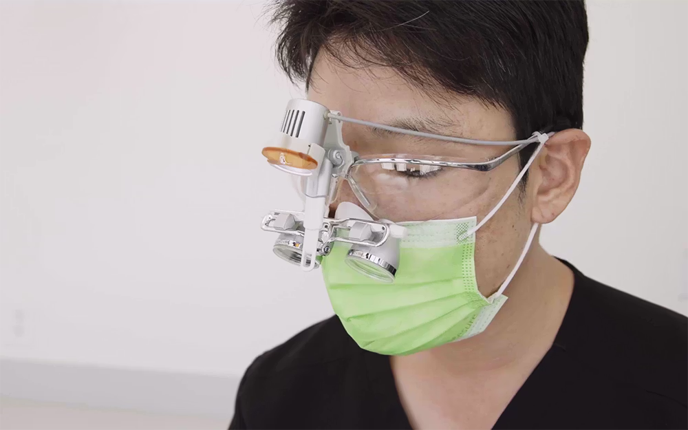 Dentist wearing a green surgical mask and magnifying glasses with attached light, used for detailed medical or dental work.