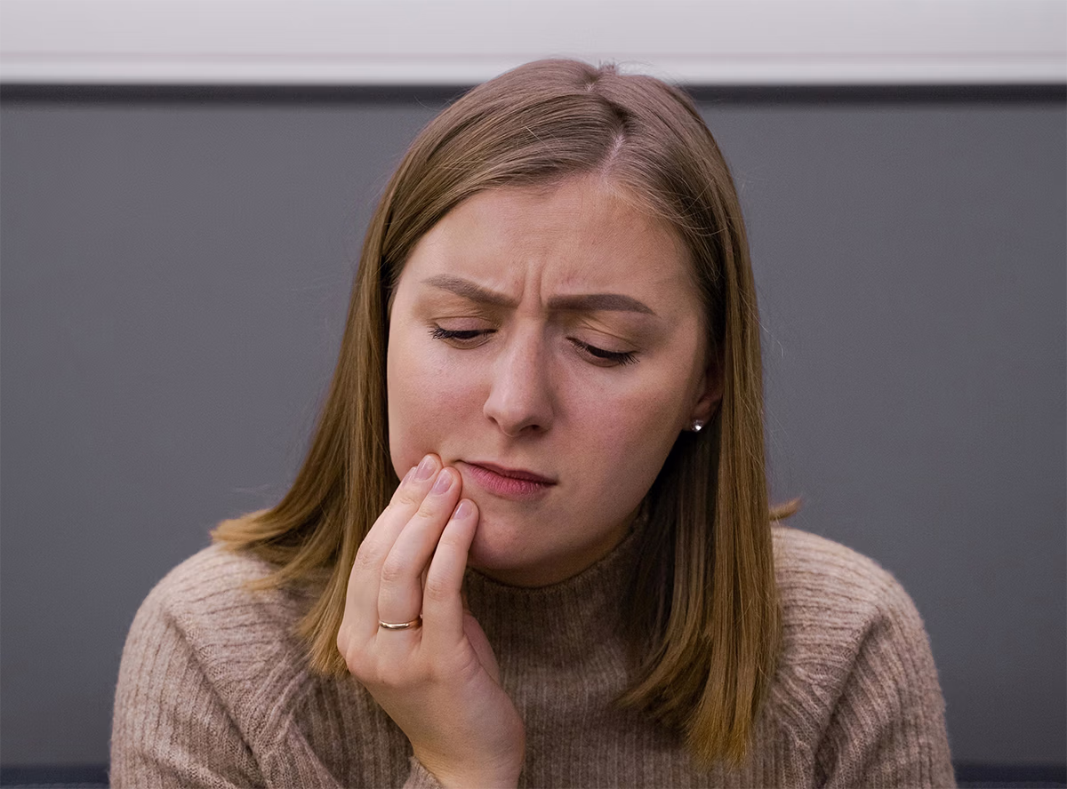 Young woman with brown hair sitting in dental office with extreme tooth pain.