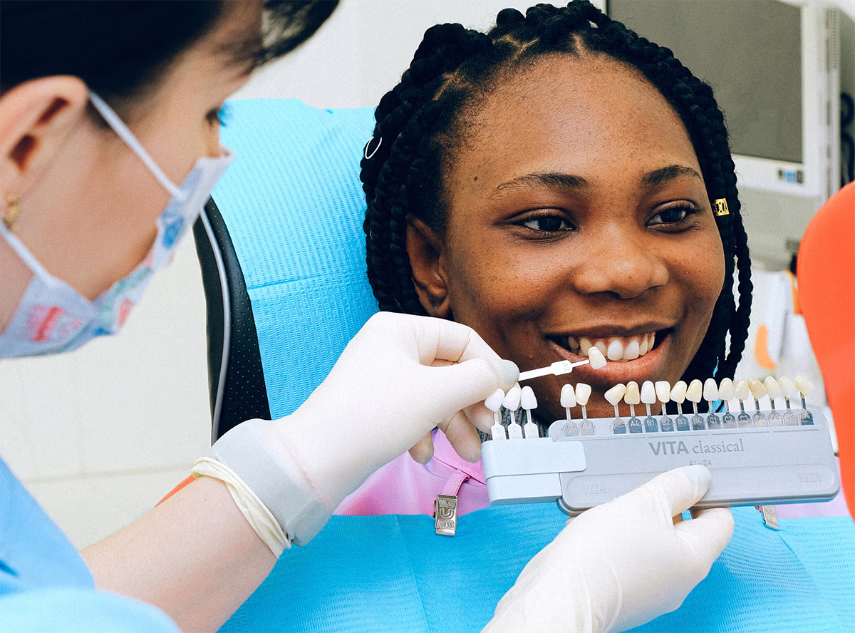 Dentist holding a shade guide next to a smiling patient's teeth for color matching.