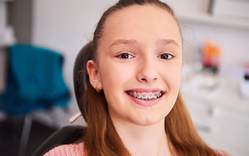 Smiling teenage girl with braces sitting in a dental chair at the orthodontist's office.