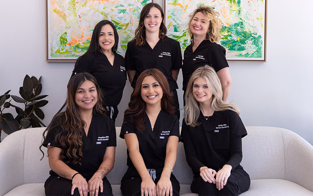 Group of six smiling women in black dental uniforms in lobby of dental office in Leander.